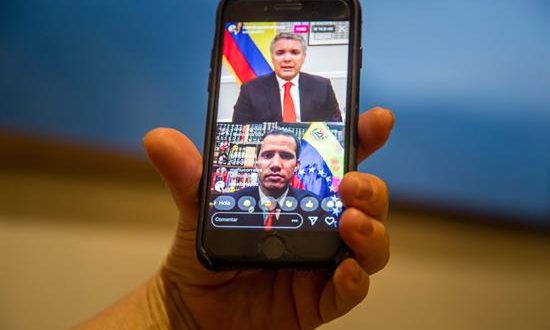 Una mujer sostiene un teléfono inteligente donde se ve una transmisión en vivo de una conversación a través de la red social Instagram entre el presidente de Colombia Iván Duque (arriba) y el jefe del Parlamento venezolano Juan Guaidó este viernes en Caracas (Venezuela). EFE