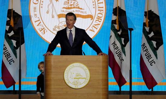 El gobernador de California, Gavin Newsom (c), habla mientras su hijo Dutch (i), de dos años, se asoma por detrás del podio tras caminar en el escenario mientras Newsom hablaba durante su ceremonia de inauguración, en el Capitolio del Estado, en Sacramento (EE.UU.). EFE/Archivo