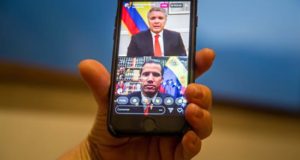Una mujer sostiene un teléfono inteligente donde se ve una transmisión en vivo de una conversación a través de la red social Instagram entre el presidente de Colombia Iván Duque (arriba) y el jefe del Parlamento venezolano Juan Guaidó este viernes en Caracas (Venezuela). EFE