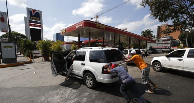 La gente empuja un automóvil sin gas a una de las pocas estaciones de combustible que tiene su propio generador eléctrico durante un apagón eléctrico en Caracas, Venezuela. Foto de archivo.
